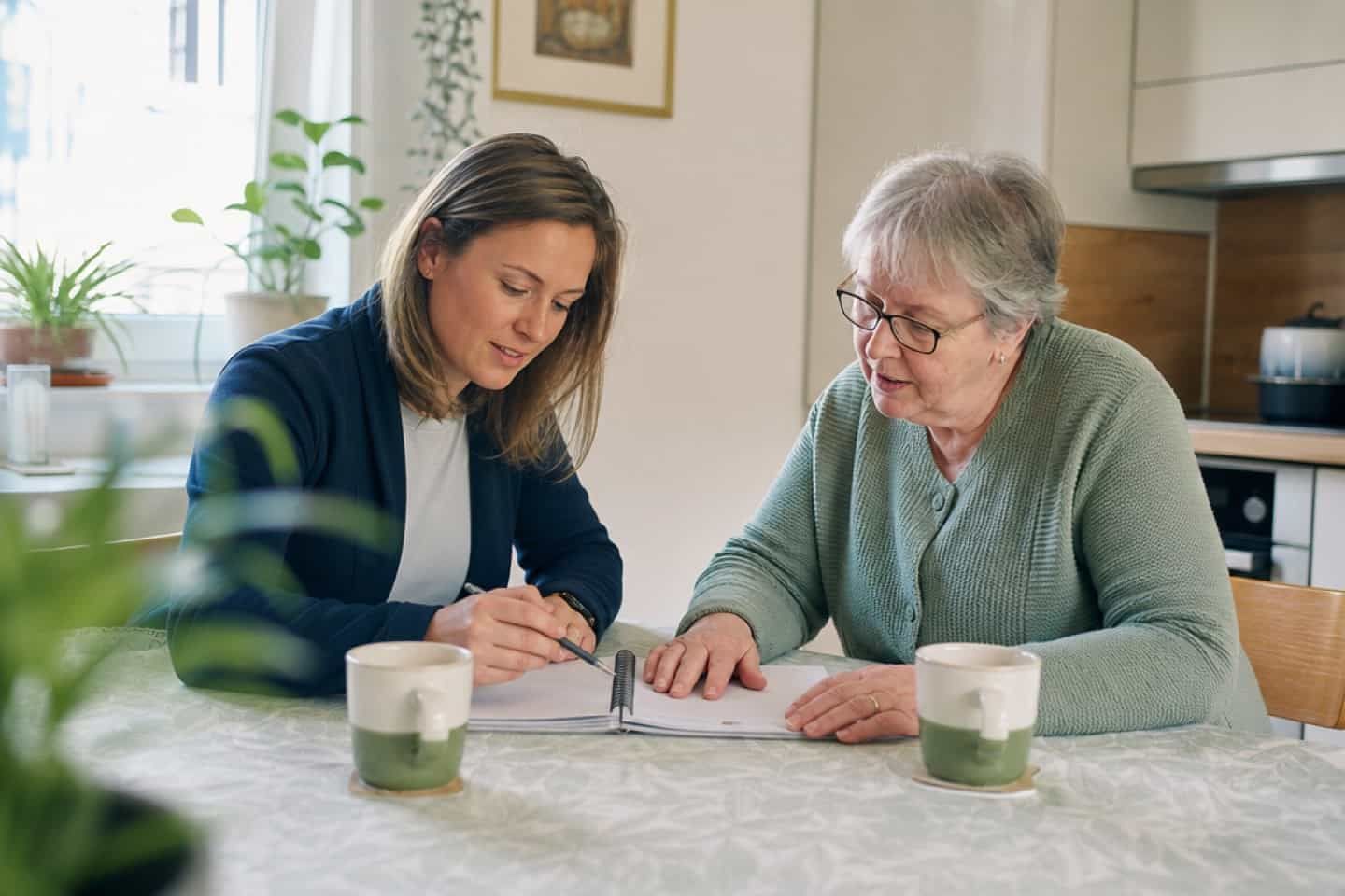 Pflegekraft und Seniorin im Gespräch am Küchentisch